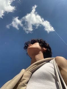 a man is looking up into the sky with a kite in his hand and clouds behind him