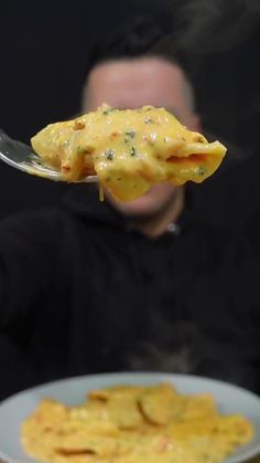 a man holding a spoon full of food over a plate with some noodles on it