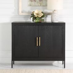 a black cabinet with two doors and a white vase on the top, in front of a painting