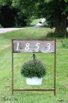 a potted plant hanging from a wooden sign in the grass with numbers on it