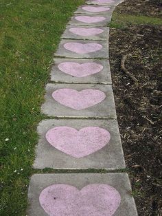 hearts painted on the sidewalk in front of some grass and dirt with blue, green, pink, and white heart stencils