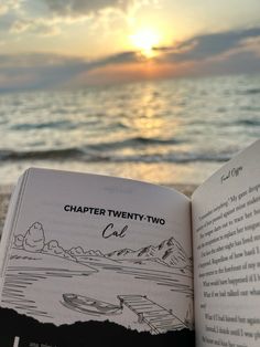 an open book sitting on top of a beach next to the ocean with a sunset in the background