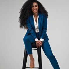 a woman sitting on top of a black stool wearing a blue suit and white shirt