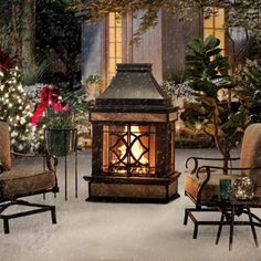 an outdoor fireplace surrounded by chairs and christmas trees with lights on them in the snow