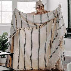 a woman is holding up a blanket in her living room with a hat on top