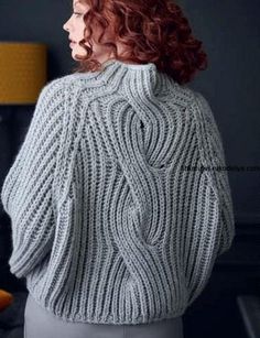 a woman with red hair wearing a gray sweater and grey pants, looking off into the distance