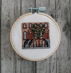 a cross - stitch pattern with a house and trees on it is hanging on a wooden wall