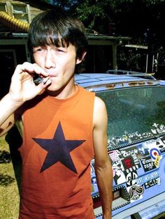 a young man standing in front of a parked car while talking on a cell phone