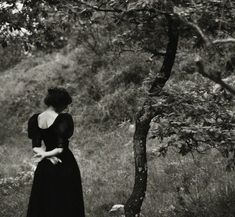 a woman in a long black dress standing next to a tree