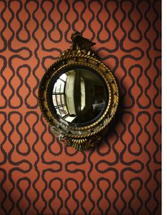 a mirror is on the wall next to a dresser and table in a room with an orange patterned wallpaper