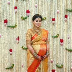 a woman standing in front of a wall with flowers on it's side and wearing a yellow saree