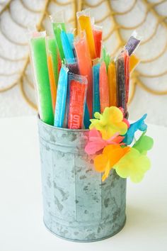 a tin can filled with candy sticks and colorful flowers on top of a white table