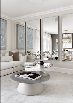 a living room filled with white furniture and mirrors on the wall above it's glass top coffee table