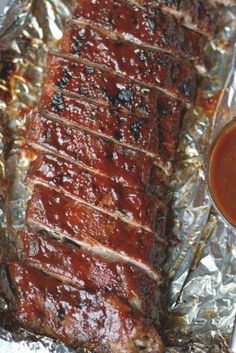 ribs covered in bbq sauce on tin foil next to a cup of ketchup