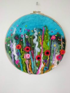 an embroidery art piece with flowers and grass in the center on a white wall hanging