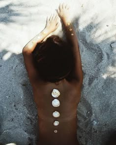 a woman laying in the sand with shells on her back