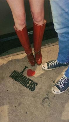 two people standing next to each other with red boots on their feet and the words i love drummers painted on the ground