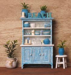 a miniature blue china cabinet with plants and dishes on it's shelf, next to a potted plant