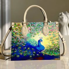 a handbag with a painting of a peacock on the front and side, sitting on a table