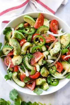 a white bowl filled with cucumber, tomatoes and onions on top of a table