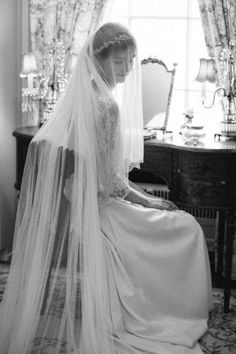 a woman in a wedding dress sitting on a chair with a veil over her head