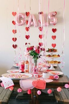 the table is set for valentine's day with pink decorations and heart shaped balloons