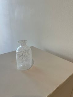 a clear glass vase sitting on top of a wooden table next to a white wall