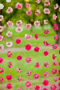 pink and white flowers hanging from strings in front of a green field with trees on the other side