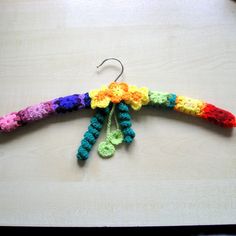 a crocheted rainbow colored flower hanging from a hook on a table with wood background