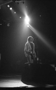 black and white photograph of a man playing guitar on stage at night with bright lights behind him