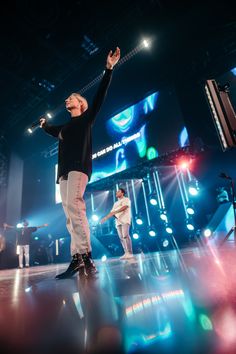 two men are performing on stage with their arms in the air and one man is holding his hand up