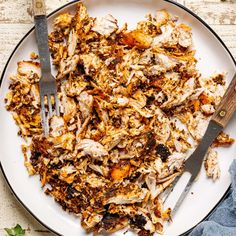 a white plate topped with meat and vegetables next to a fork on top of a table