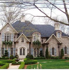 a large brick house with lots of windows and bushes on the front lawn, surrounded by lush greenery