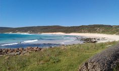 the beach is surrounded by large rocks and green grass, with blue water in the background