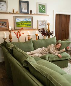 a woman laying on top of a green couch in a living room next to candles