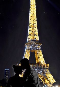 two people standing in front of the eiffel tower at night with their backs to each other