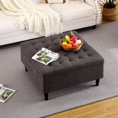 a living room with a gray ottoman and magazines on the floor