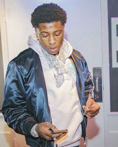 a young man in a black jacket looking at his cell phone while standing next to a door