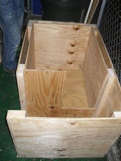 a large wooden box sitting on top of a green floor next to a wire fence