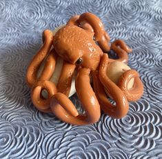 an orange octopus toy is laying on a blue patterned tablecloth with wavy waves in the background