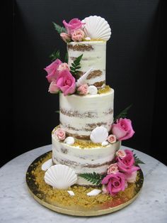 a three tiered wedding cake with pink flowers and seashells on the side