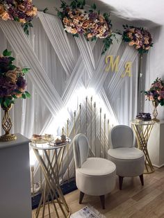 chairs and tables with flowers on them in front of a backdrop