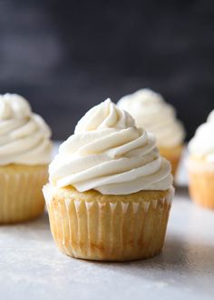 three cupcakes with white frosting sitting on a table