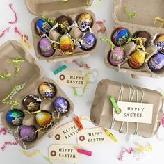 an assortment of decorated easter eggs in cardboard boxes with tags on them, sitting on a table