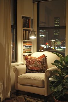 a living room with a chair, potted plant and bookshelf in the window