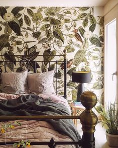 a bed sitting next to a window in a bedroom under a wallpapered mural