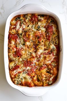 a white casserole dish filled with pasta and vegetables on a marble countertop