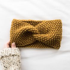 a hand holding a knitted headband on top of a white bed next to a pair of gloves