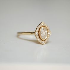 a yellow gold ring with an oval cut diamond surrounded by small white diamonds