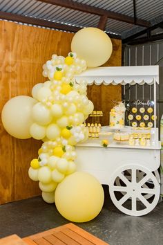 a dessert cart with balloons and cupcakes on the table in front of it